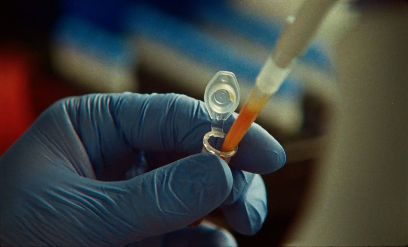 A gloved hand pipetting into a small tube in a lab